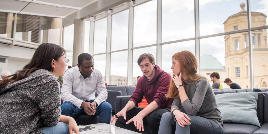 A group of students sit at a table writing equations in the Maths building; the Radcliffe Observatory is visible out the window in the background. 