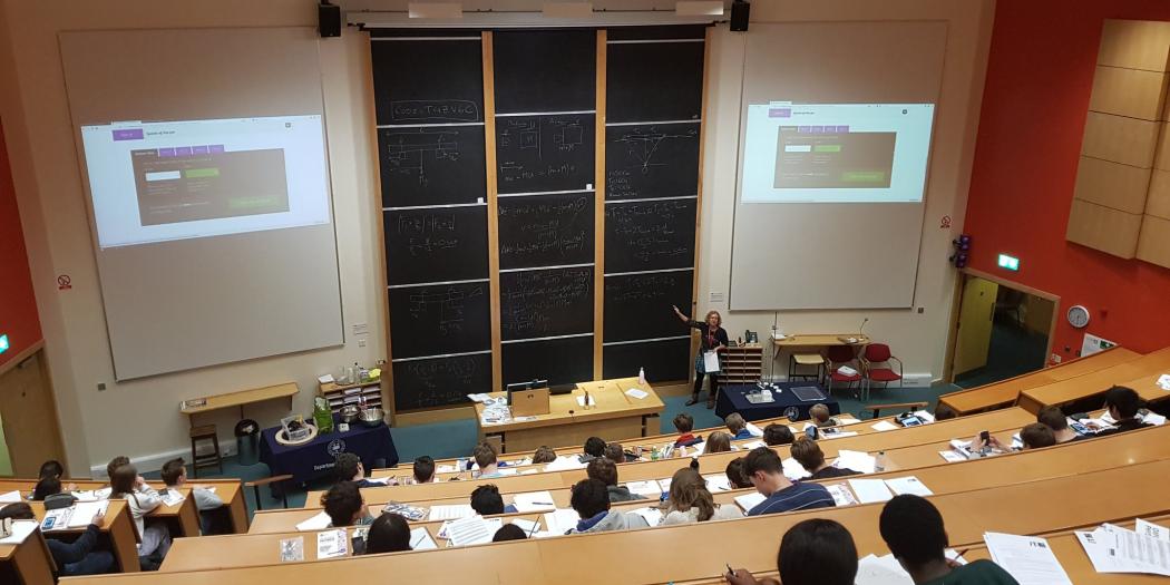 A physics lecture from behind, with a panel of 9 blackboards showing equations and writing.