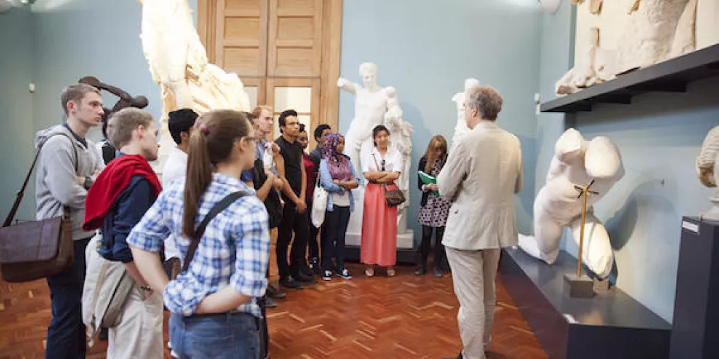 a group of classics students listen to a guide in the Ashmolean Museum.