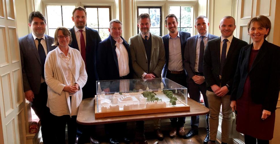 A group from Trinity College and contractors Gilbert Ash stand next to a model of the new Levine Building after signing a contract.