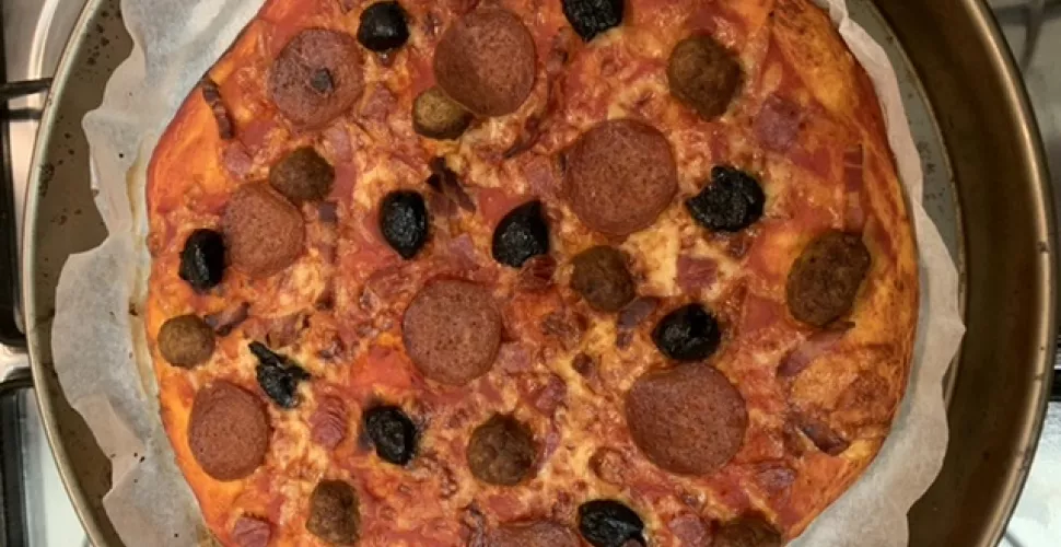 A home cooked pizza on a pan with pepperoni and olives.