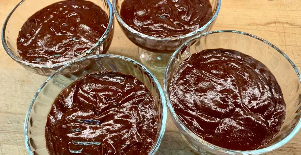 Four bowls of chocolate mousse sit on a table.