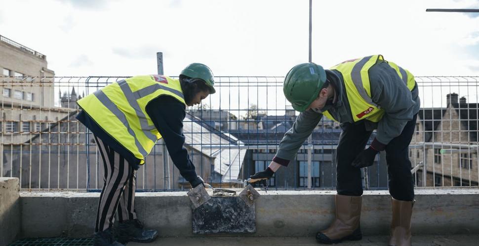 Two Trinity College students trowel the final cement onto the Levine Building.