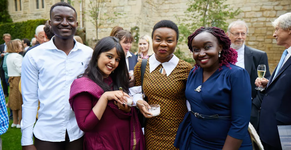 Four trinity postgraduates pose at a reception in the college President's Garden.