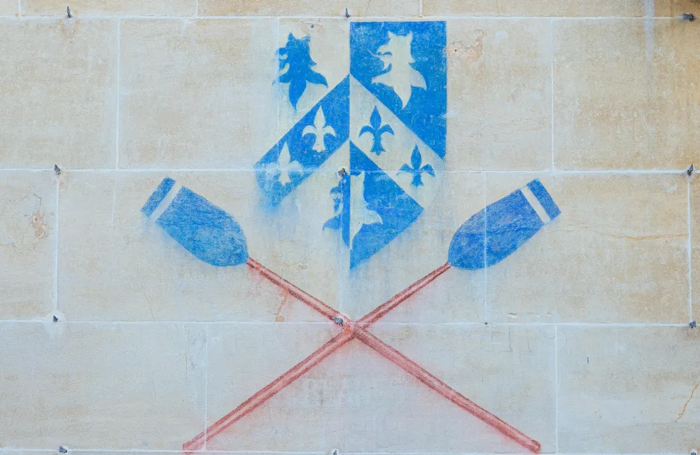 A chalked image of the Trinity College shield with boat club blades on the wall of a college building.
