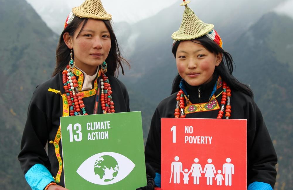 Two girls in Bhutan hold up signs saying 'climate action' and 'no poverty'.