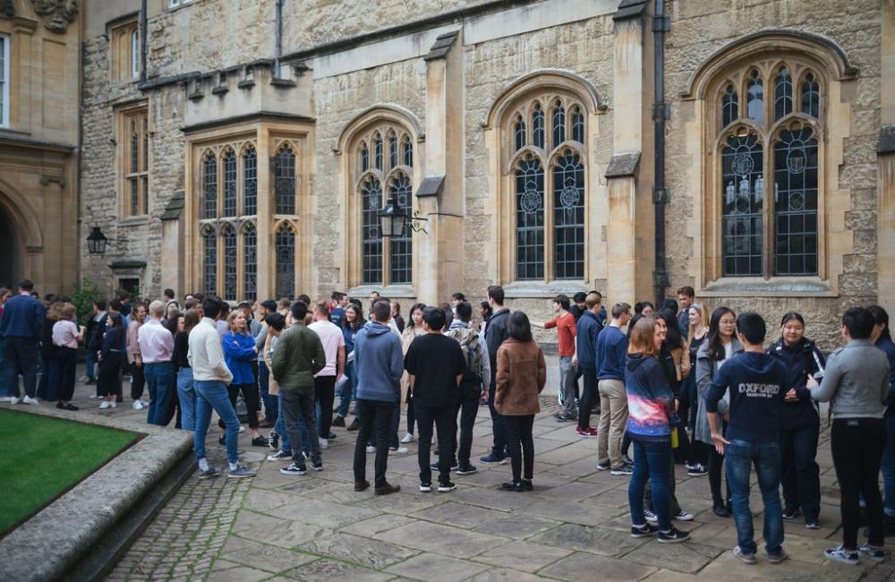 A large group of students stand talking outside the Trinity College dining hall.