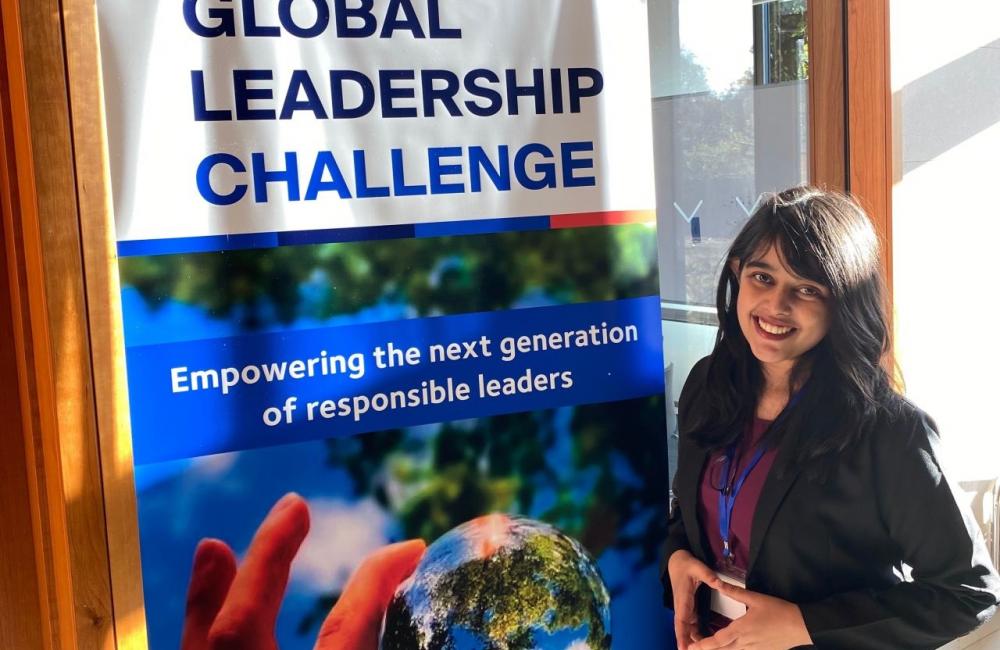 Trinity student Rai Sengupta stands in front of a banner that reads 'Global Leadership Challenge.'