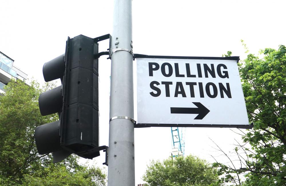 A traffic light pole with a polling station sign attached to it in London, May 2022