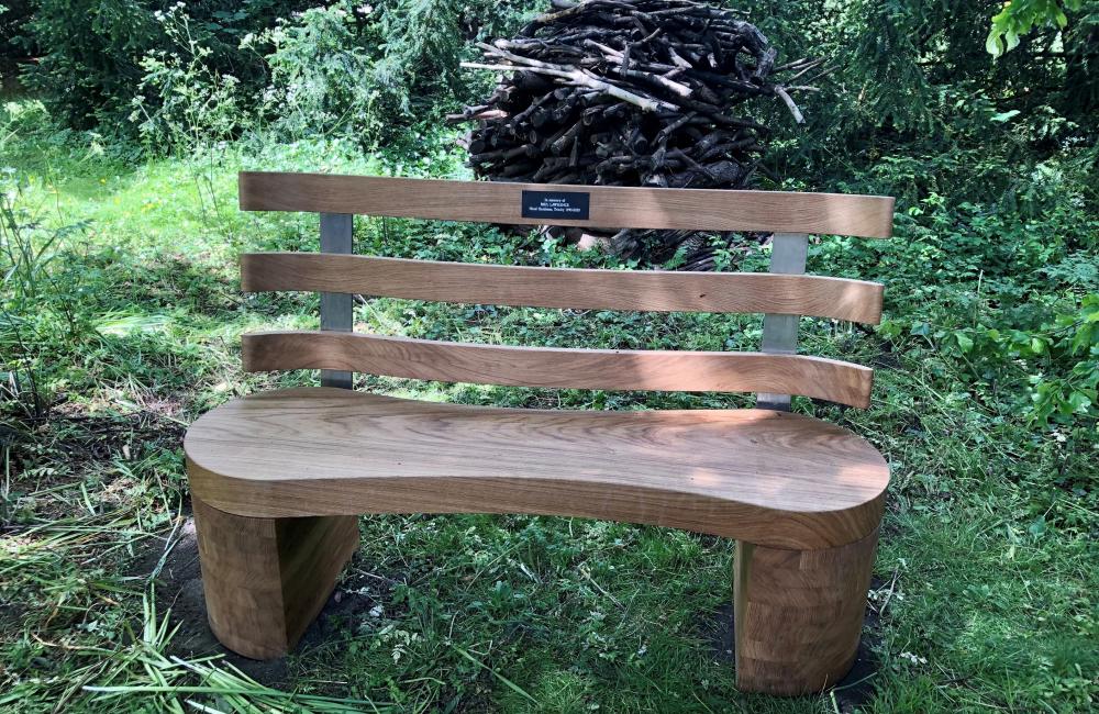 A wooden bench dedicated to Paul Lawrence sits in the Trinity College gardens.