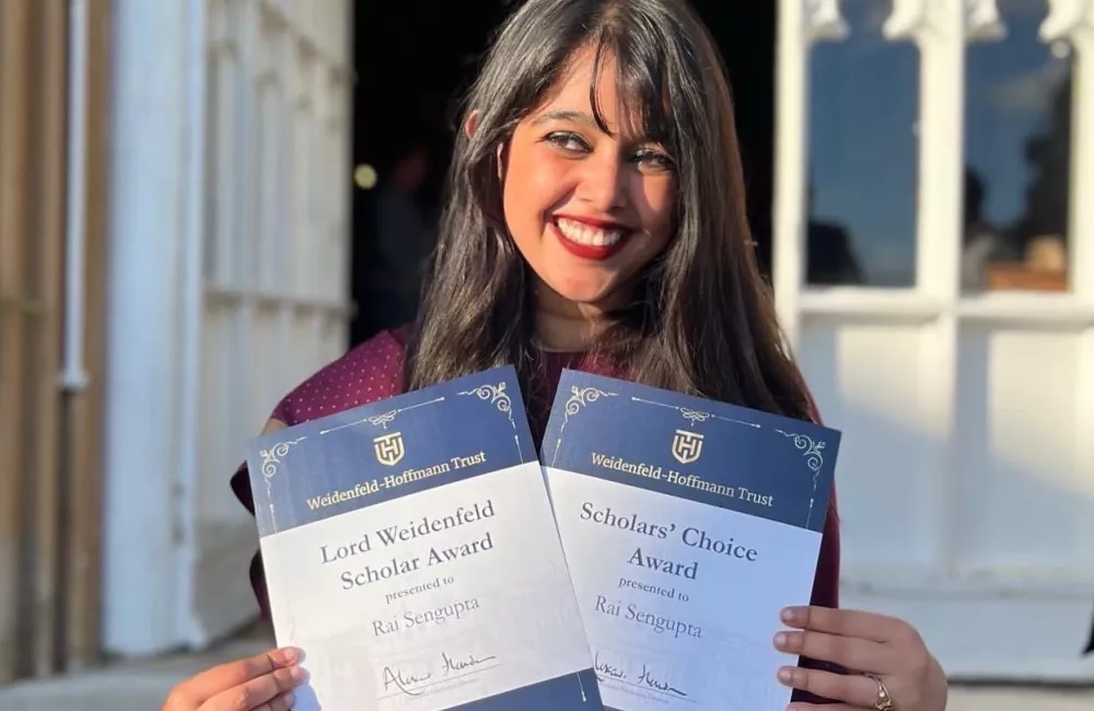 Rai Sengupta stands holding two awards from the Weidenfeld-Hoffmann Trust.