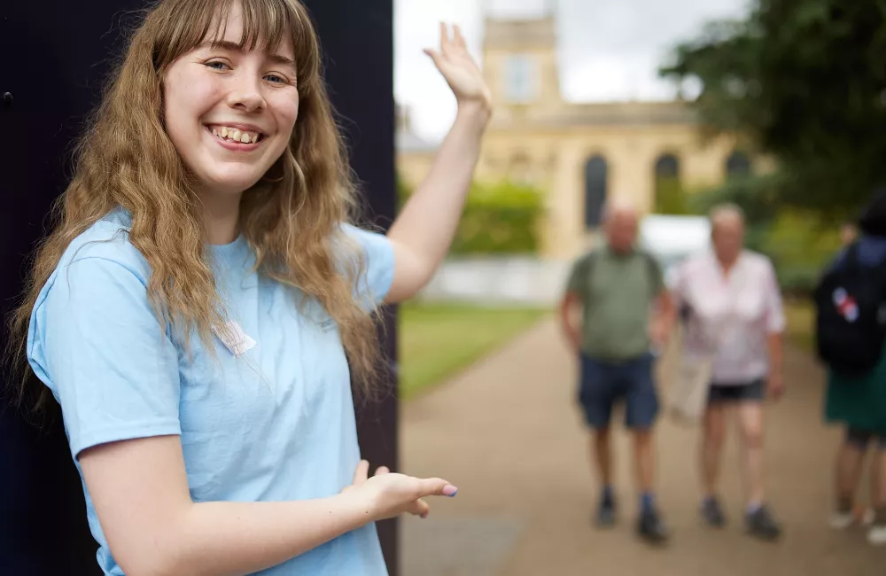 A student stands at the front gate of Trinity college welcoming visitors in.