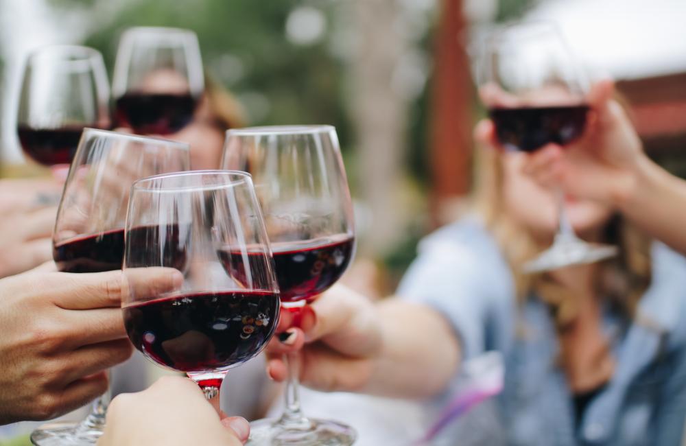 People hold red wine glasses together to cheers 
