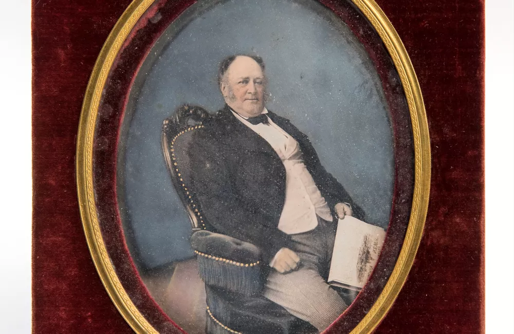 A hand-painted half-plate daguerreotype in green leather case of Seated man holding a copy of the Illustrated London News, c. 1850 