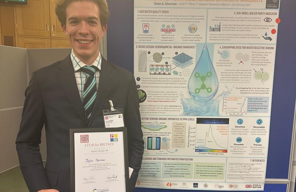 Dylan Sherman stands at the STEM for Britain event in front of his prize-winning poster. He holds his medal citation.