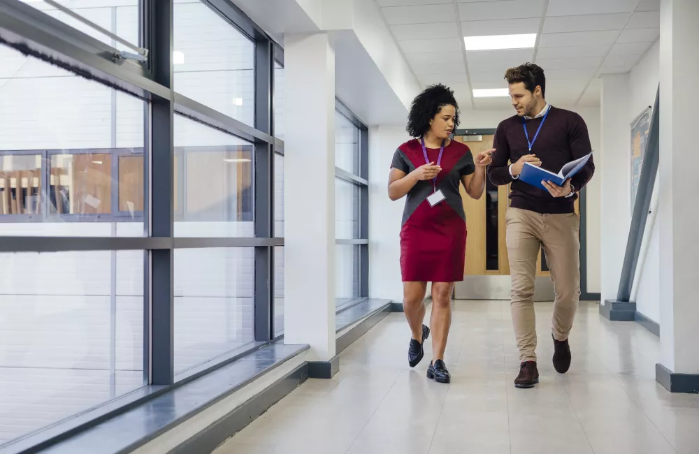 Two teachers walk down a school hallway chatting.