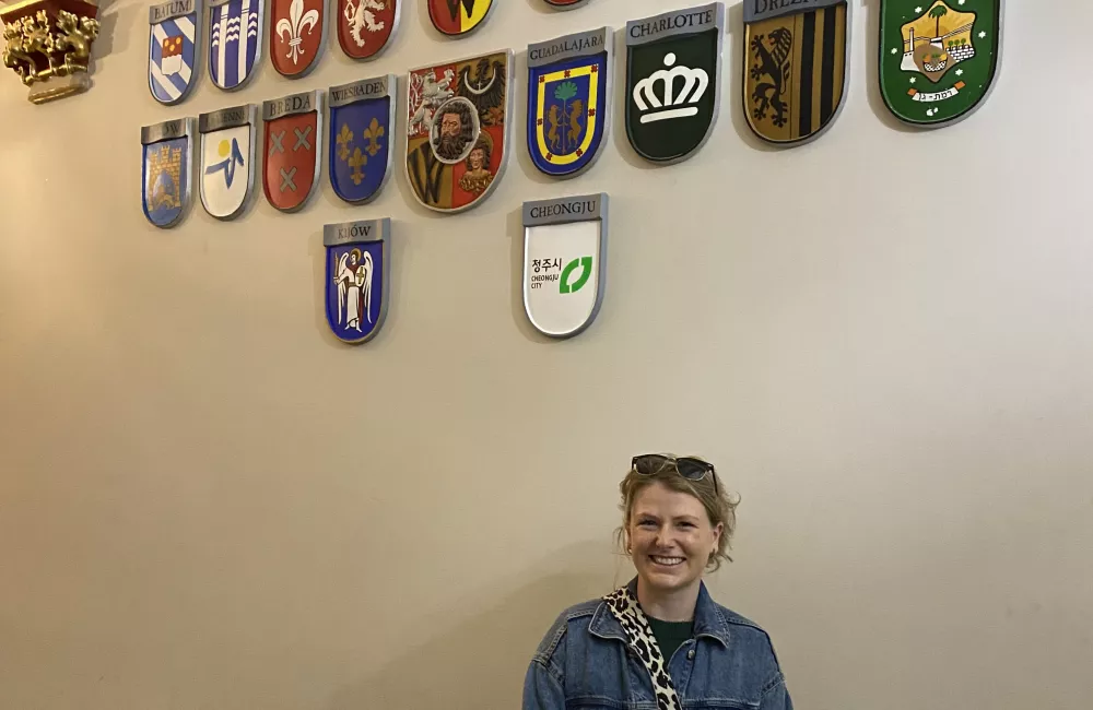 Trinity student Ishbel Henderson stands in a building with a bunch of European country shields on the wall.