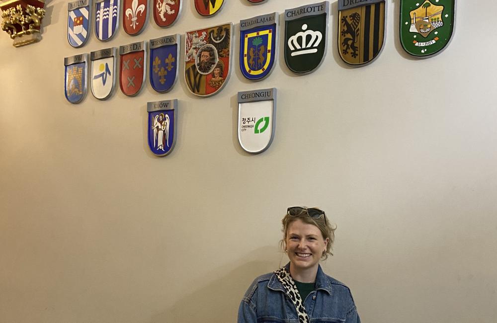 Trinity student Ishbel Henderson stands in a building with a bunch of European country shields on the wall.