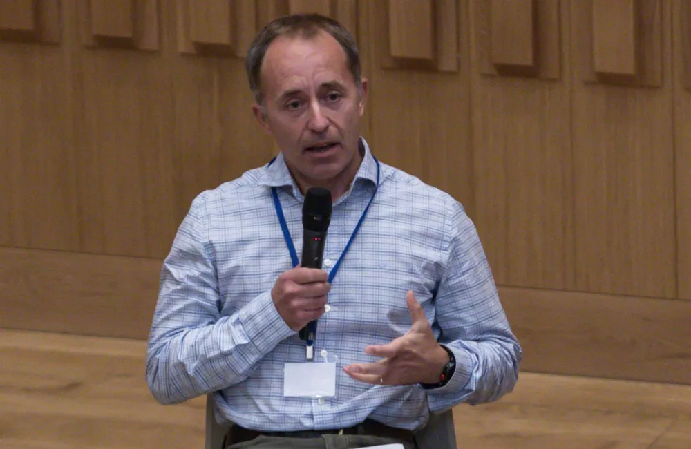 Tom Drew sits with a microphone talking.