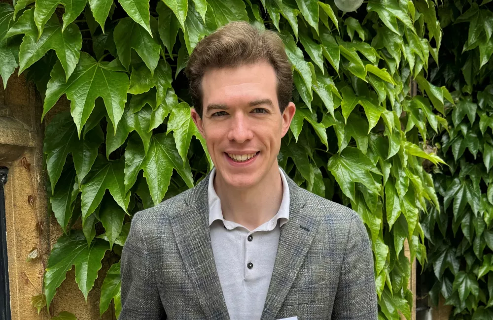 Dylan Sherman stands holding a certificate confirming he won the Three-Minute Thesis competition at Oxford.
