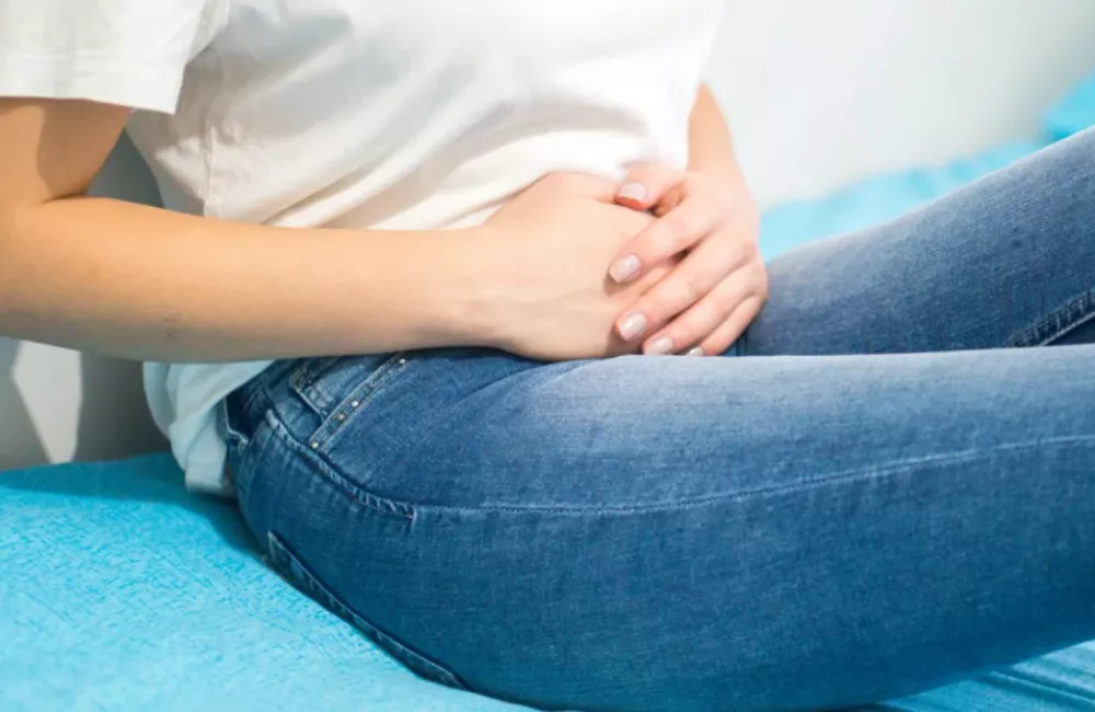A woman holds her midsection while sitting on a blue couch.