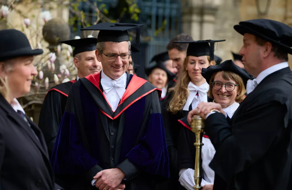 Trinity Fellow Nick Barber stands in a gown and cap with other members of college preparing for the ceremony to admit him as Senior Proctor.