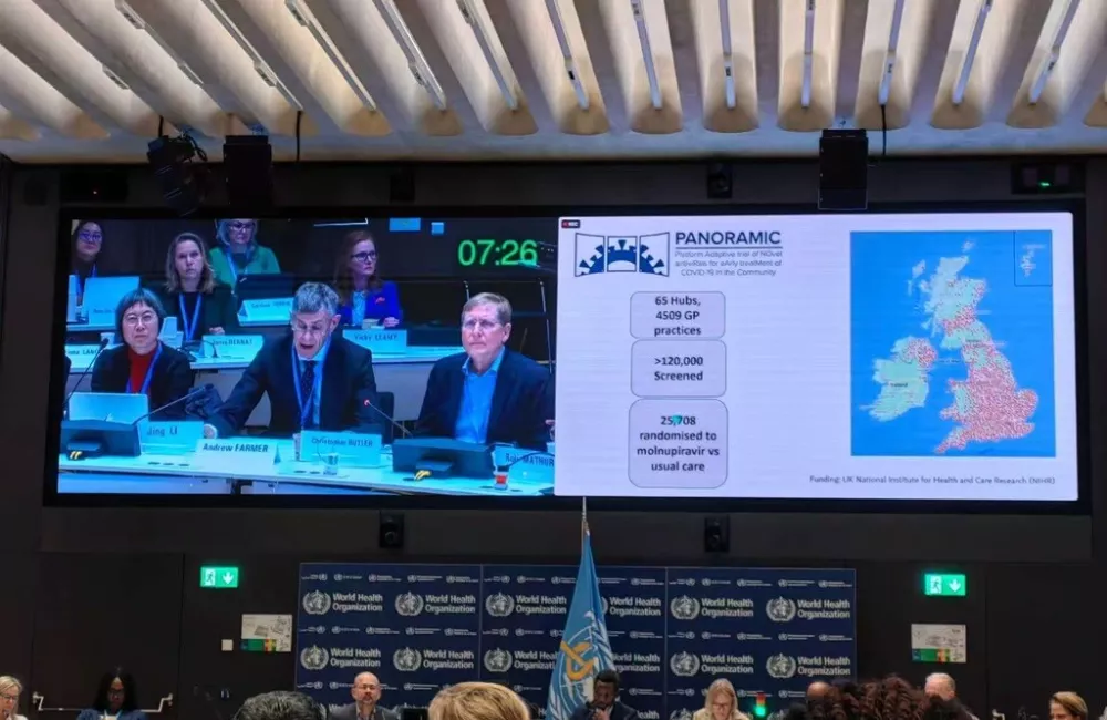 Christopher Butler sits in a session at the World Health Organisation showing slides on a screen about the PANORAMIC covid-19 trial.