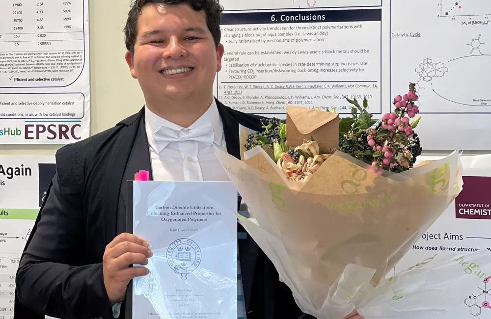 Trinity DPhil student Kam Poon stands holding flowers after his doctoral dissertation defence.