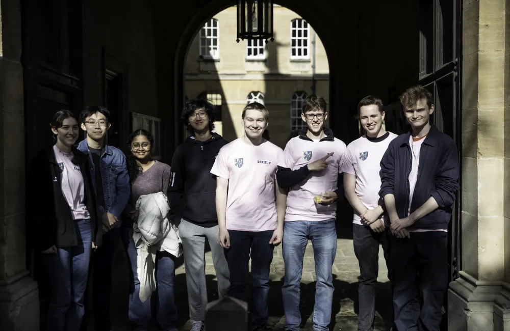 A group of Trinity undergraduates in pink shirts stand in the college's chapel archway on moving-in day. 