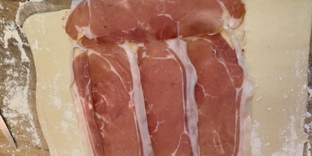 Parma ham slices lined up on a sheet of puff pastry.