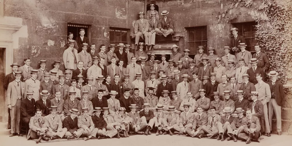 A black and white image of Trinity College students from 1899 sat in a quad.