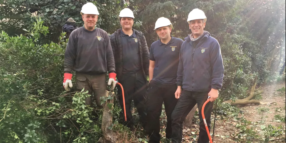 Four members of the Trinity College gardens team stand with hard hats and saws during tree clearing.