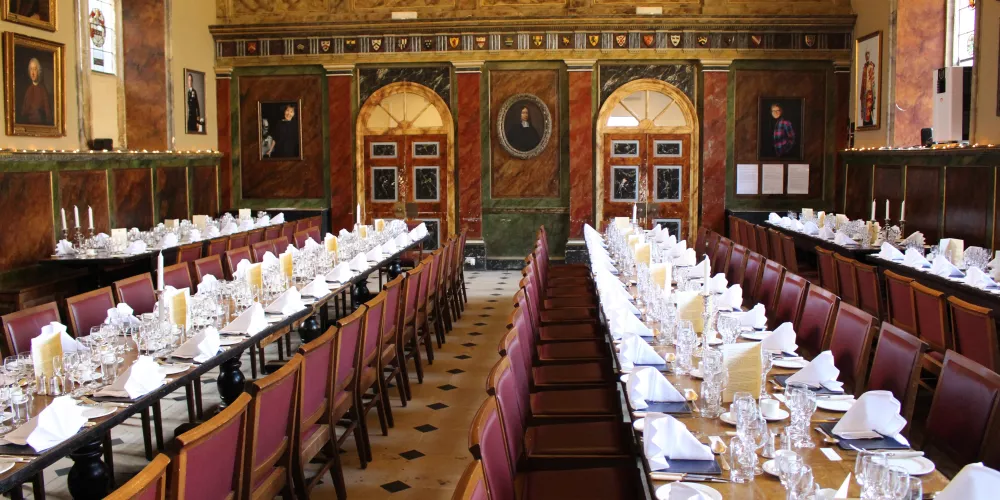 A view of the Trinity dining hall with long tables set for a dinner.