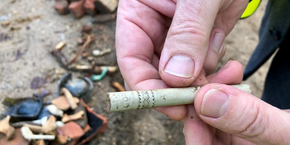 A hand holds a clay pipe stem dug up on site.