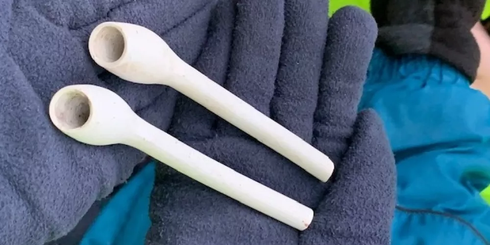 Two small clay pipes in the gloved hands of an excavation archaeologist.