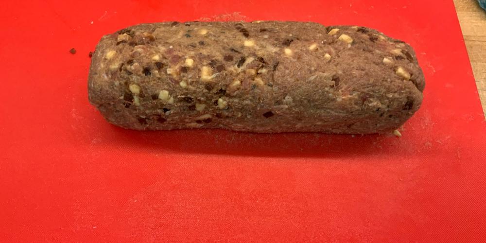 a rolled up log of sausage meat on a red chopping board.