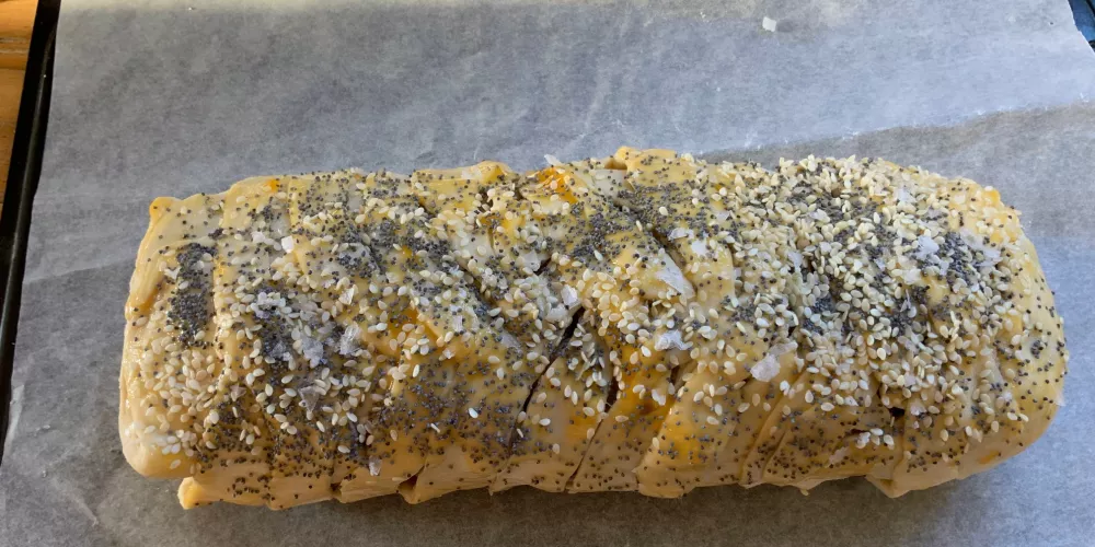 A sausage slice ready to go in the oven with seeds on top.