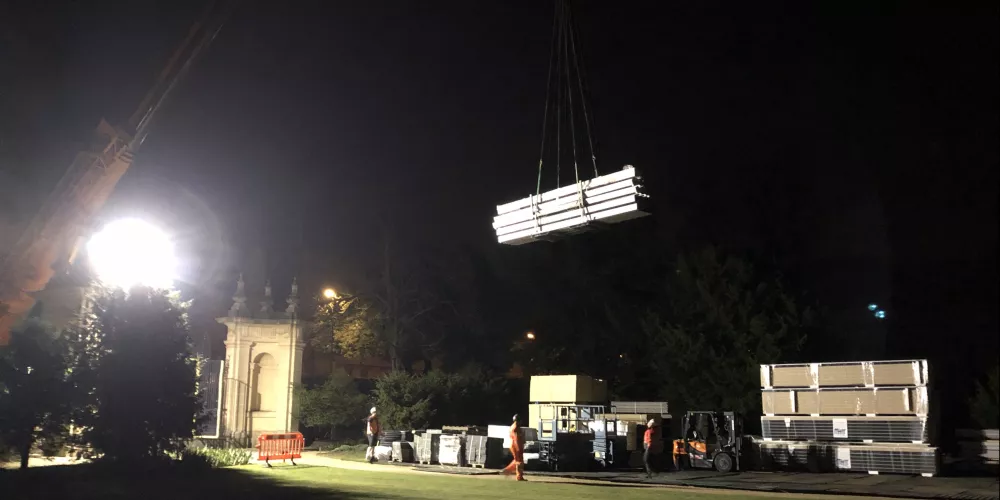 A view from the Trinity lawns of a crane lifting huge building parts over the gates.