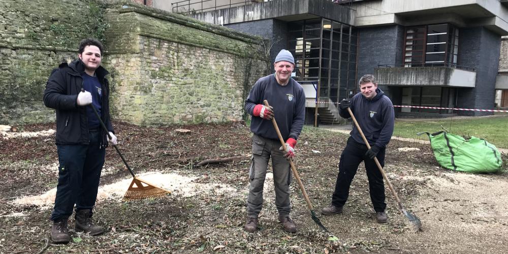three members of the Trinity College gardens team with rakes clear away the site.