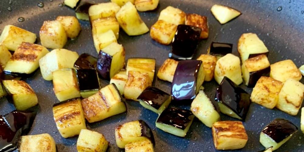 A pan with aubergine cubes frying.