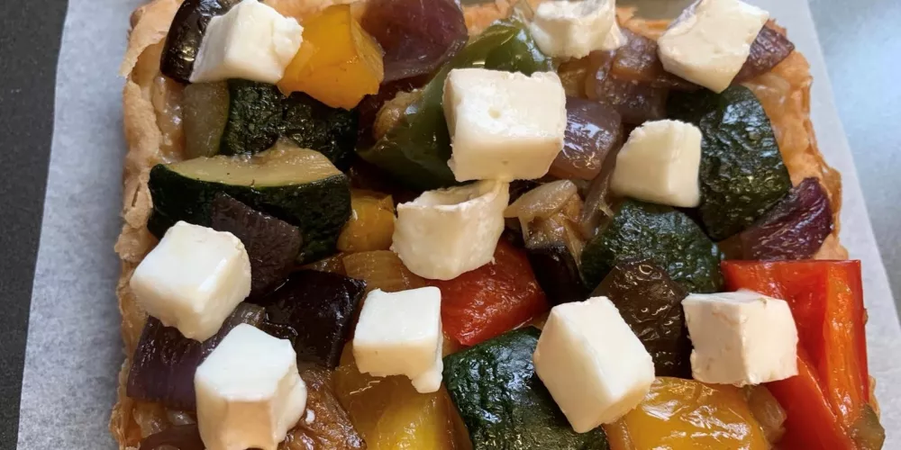 An assembled tart with vegetables and cheese cubes ready to be cooked.