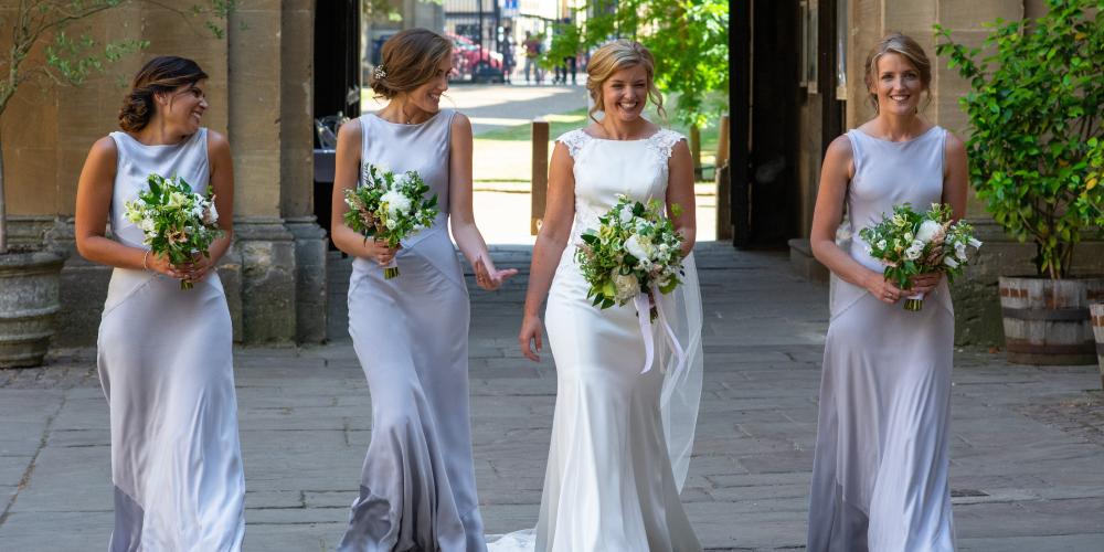A bride and bridesmaids holding bouquets walk into college from the main gate.