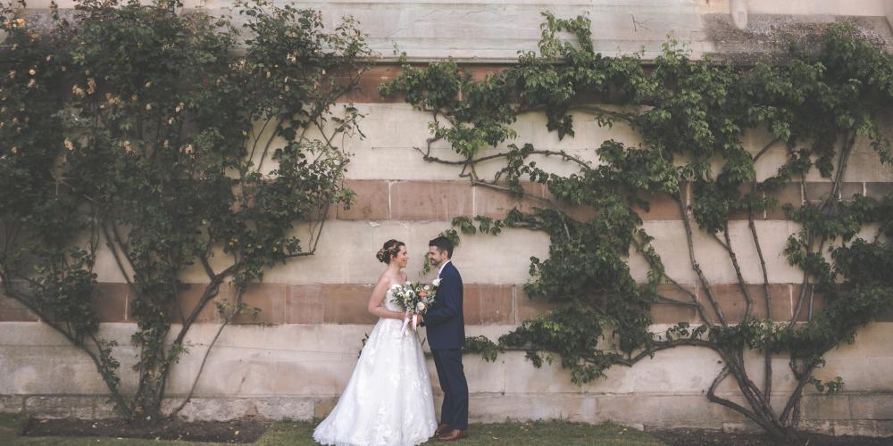 A wedding couple stand in profile against the brick wall and rose plants in Trinity's front quad.