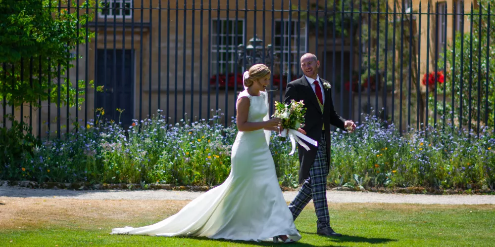 A wedding couple stroll on the Trinity lawn in front of Garden quad.