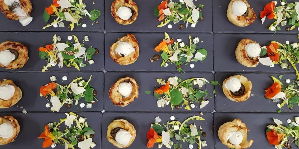 An image from above of plated apple tart tatin with oxford blue sorbet, pickled walnut and nasturtium salad.