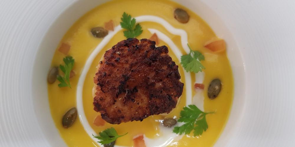 A plated bowl of butternut squash soup with seared scallop, wilted spinach and cajun spiced pumkin seeds.