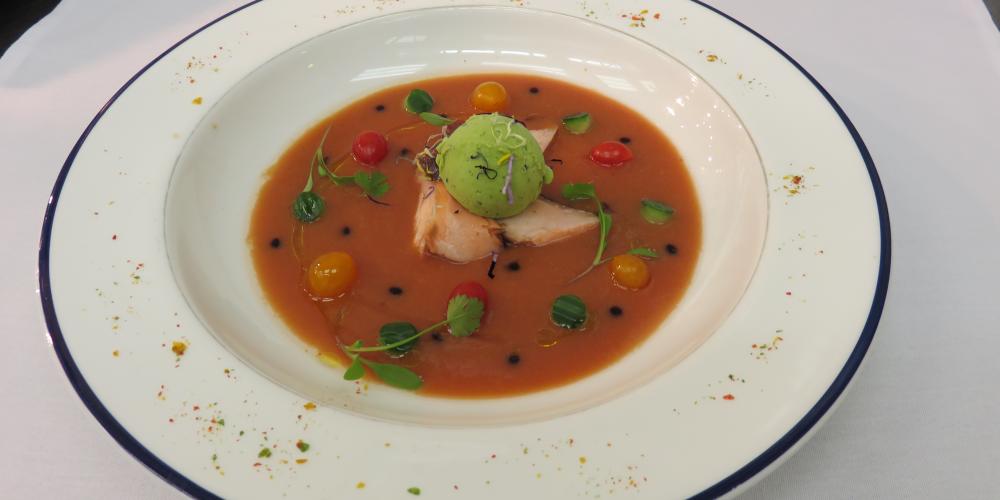 A bowl of gazpacho soup with oak roast salmon, avocado sorbet, balsamic vinegar and olive oil.
