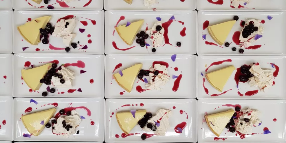 A dozen plates of lemon and white chocolate tart with pavlova, blueberry sorbet and compote.