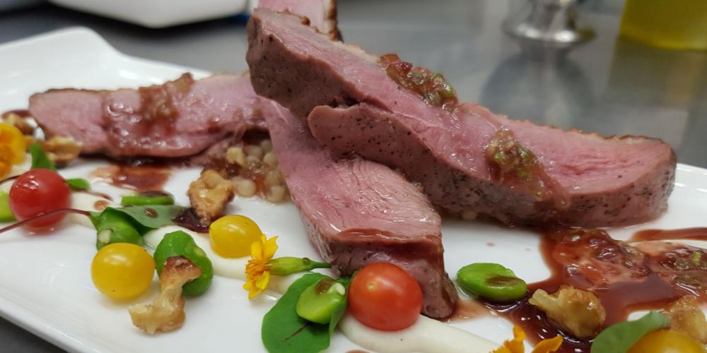 A close-up of a dish of seared duck supreme with amarena cherries, walnut couscous and cardamom oil.