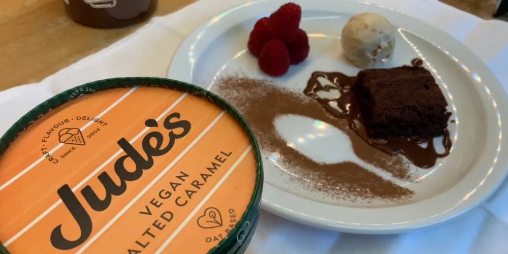 a plate of vegan brownie, raspberries and ice cream next to a tub of Jude's vegan dairy-free salted caramel ice cream.